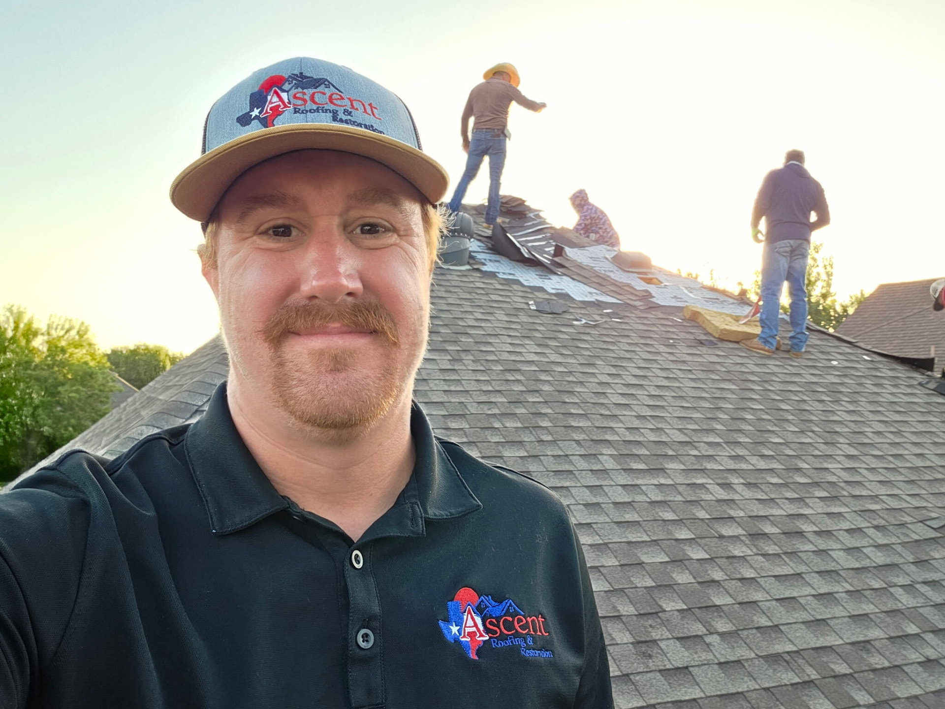 Ascent team member in branded clothing with a roofing crew working behind him